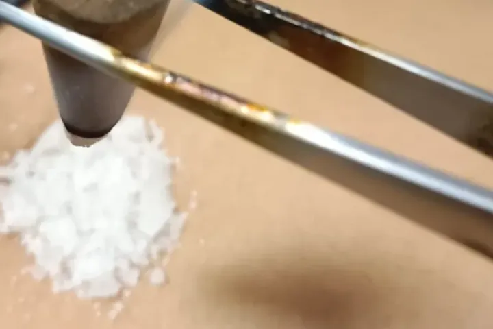 Un cône d’encens tenu à la pince au-dessus d’un petit tas de sel, pendant une chauffe ombilicale