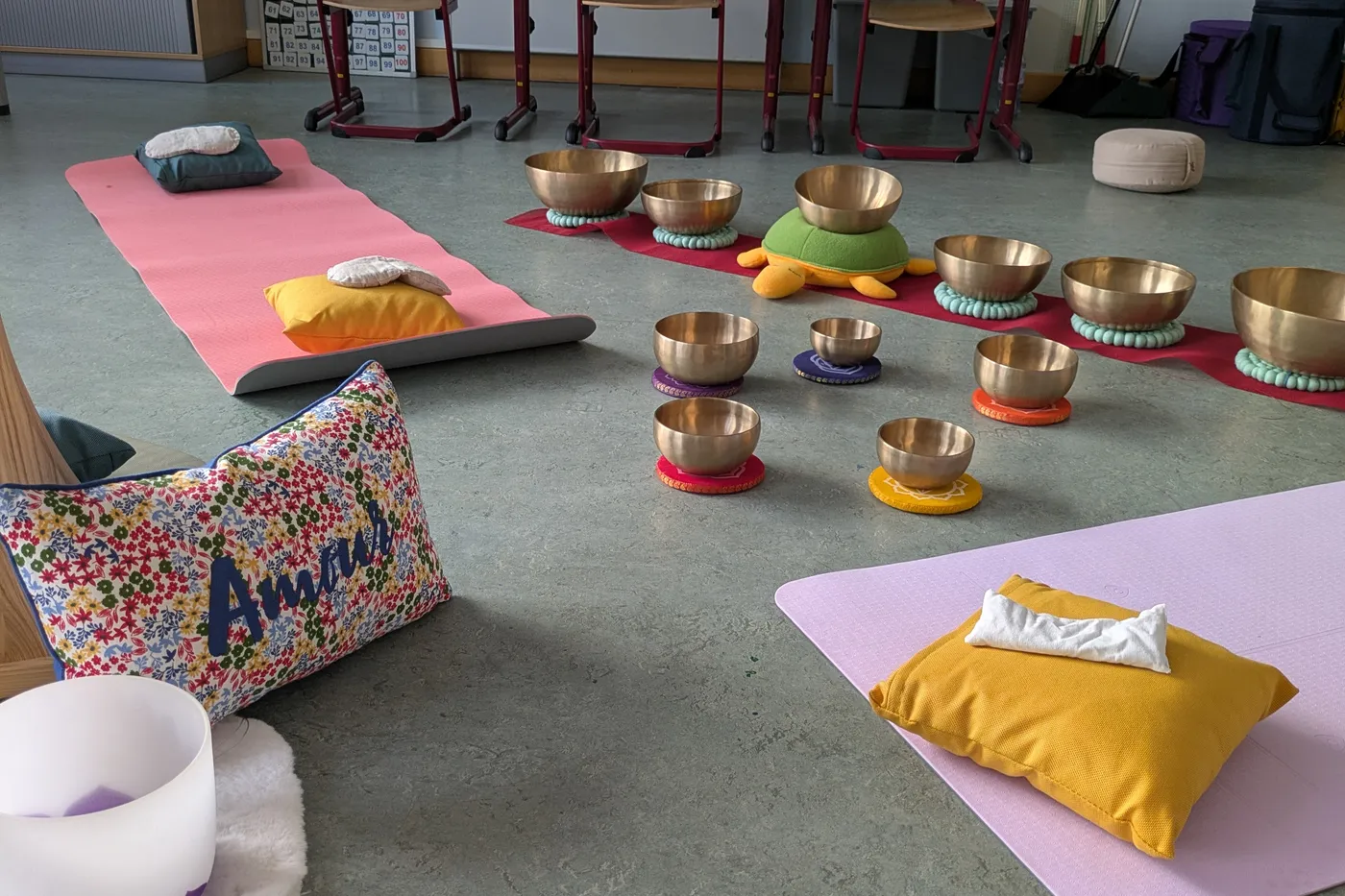 Une salle de classe préparée : des tapis au sol, des coussins, et les bols chantants posés autour.