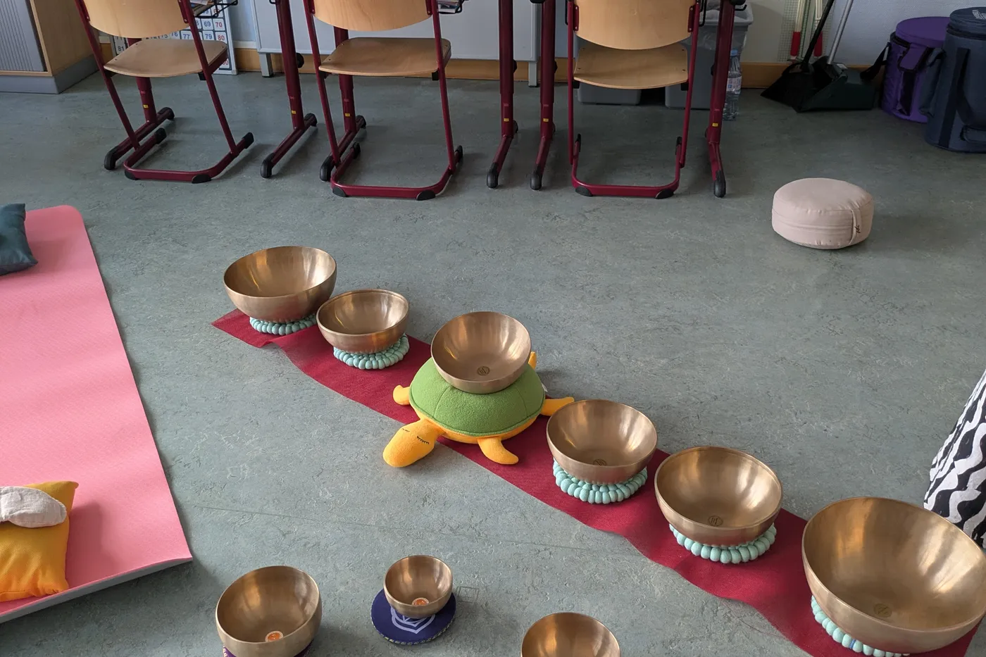 Les bols chantants alignés sur un tapis, devant les tables empilées de la classe.