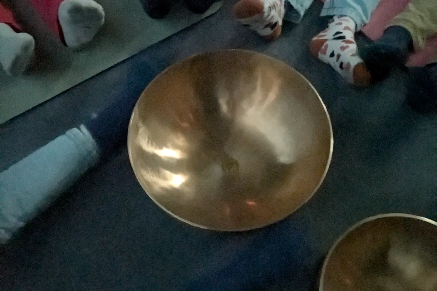 Des mains d’enfants tendues autour d’un grand bol chantant posé au sol.